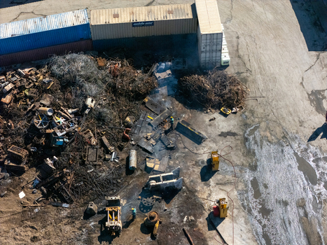 Aerial view of a scrap metal recycling yard with piles of discarded metal industrial machinery shipping containers and workers on the ground in Carson California United States.