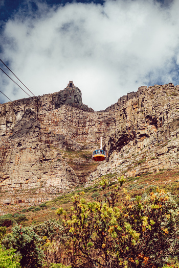 View of Table Mountain with the aerial cableway car ascending the rugged sandstone cliffs under a cloudy sky in Cape Town Western Cape South Africa. View of Table Mountain with the aerial cableway car ascending the rugged sandstone cliffs under a cloudy sky in Cape Town Western Cape South Africa.