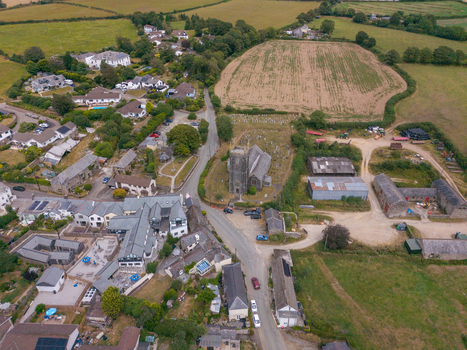 Aerial view of a historic stone church and its graveyard surrounded by rural fields farm buildings and residential houses in the countryside of Looe Cornwall United Kingdom. Aerial view of a historic stone church and its graveyard surrounded by rural fields farm buildings and residential houses in the countryside of Looe Cornwall United Kingdom.