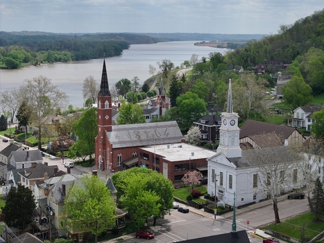 Aerial view of historic churches and residential houses along the Ohio River with lush green trees under a cloudy sky in Aurora Indiana United States. Aerial view of historic churches and residential houses along the Ohio River with lush green trees under a cloudy sky in Aurora Indiana United States.