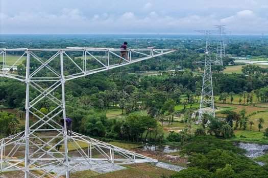 Trishal Upazila Bangladesh 13 May 2026 Aerial view of workers on a high voltage electricity pylon overlooking lush green fields and rural landscape. Trishal Upazila Bangladesh 13 May 2026 Aerial view of workers on a high voltage electricity pylon overlooking lush green fields and rural landscape.