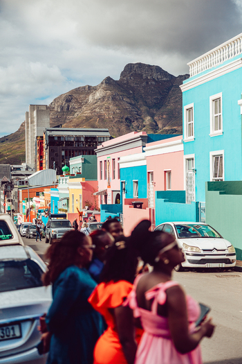 View of the colorful houses in Bo Kaap with people on the street and Table Mountain under a cloudy sky Cape Town Western Cape South Africa. View of the colorful houses in Bo Kaap with people on the street and Table Mountain under a cloudy sky Cape Town Western Cape South Africa.