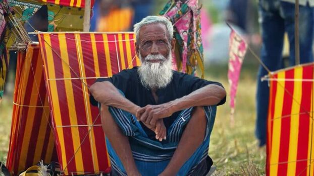 View of an elderly man sitting among colorful kites in Bangladesh. View of an elderly man sitting among colorful kites in Bangladesh.