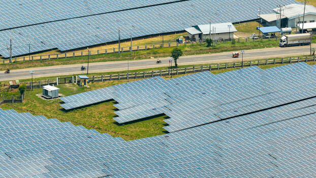 Bais City Negros Island Region Philippines 20 September 2026 Aerial view of a solar farm with rows of photovoltaic panels a nearby road with vehicles and small utility buildings.