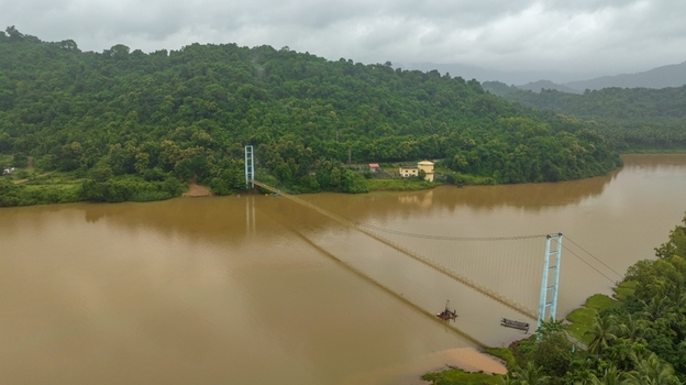 Aerial view of the suspension bridge spanning the Sharavathi river surrounded by lush green hills and dense vegetation under a cloudy sky in Honnavar Karnataka India.