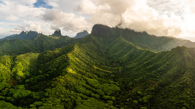 Aerial view of the lush volcanic peaks of Moorea and dense tropical forests under a cloudy sky in Moorea Maiao Windward Islands French Polynesia. Aerial view of the lush volcanic peaks of Moorea and dense tropical forests under a cloudy sky in Moorea Maiao Windward Islands French Polynesia.