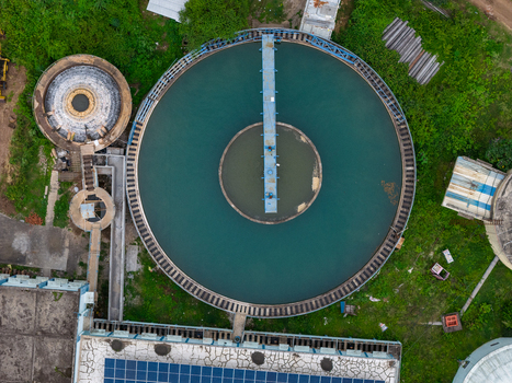 Aerial view of a circular water treatment sedimentation tank with a central bridge and surrounding green vegetation and solar panels in Karad Maharashtra India.