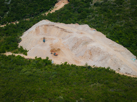 Aerial view of a large quarry with an excavator and truck working on a pile of light colored stone surrounded by dense green forest Jala Vlore County Albania. Aerial view of a large quarry with an excavator and truck working on a pile of light colored stone surrounded by dense green forest Jala Vlore County Albania.