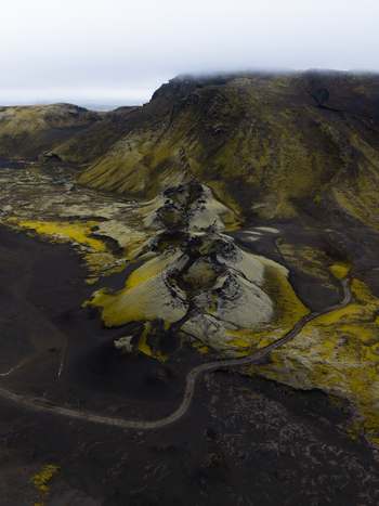 Aerial view of stark volcanic terrain where moss covered rocks meet black sand under a cloudy sky creating a surreal landscape Lakagigar Iceland. Aerial view of stark volcanic terrain where moss covered rocks meet black sand under a cloudy sky creating a surreal landscape Lakagigar Iceland.