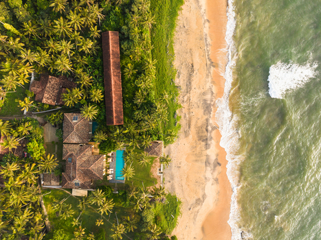 Aerial view of a tropical resort with a swimming pool nestled among palm trees along a sandy beach and turquoise ocean waves Galle Southern Province Sri Lanka.