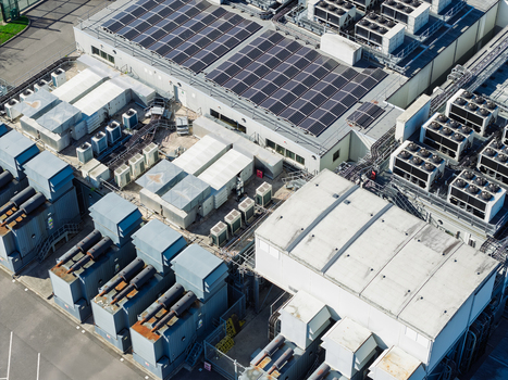 Aerial view of a modern data center facility featuring extensive rooftop solar panels numerous industrial cooling units and electrical infrastructure in the United Kingdom.