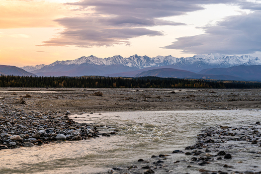 View of the Gerstle River flowing through a rocky landscape with snow capped mountains in the background under a soft sunset sky in Deltana Alaska United States. View of the Gerstle River flowing through a rocky landscape with snow capped mountains in the background under a soft sunset sky in Deltana Alaska United States.