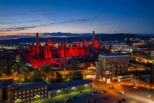 Volklingen Germany 09 May 2026 Aerial view of the Volklingen Ironworks illuminated with red lights at dusk featuring industrial chimneys and the surrounding urban landscape. Volklingen Germany 09 May 2026 Aerial view of the Volklingen Ironworks illuminated with red lights at dusk featuring industrial chimneys and the surrounding urban landscape.