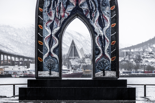 View of the Arctic Cathedral framed by a colorful mosaic archway with snowy mountains in the background in Tromso Troms Norway. View of the Arctic Cathedral framed by a colorful mosaic archway with snowy mountains in the background in Tromso Troms Norway.