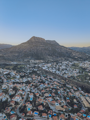Aerial view of the Penon de Ifach mountain rising above residential neighborhoods with terracotta rooftops and swimming pools in Calp Valencian Community Spain. Aerial view of the Penon de Ifach mountain rising above residential neighborhoods with terracotta rooftops and swimming pools in Calp Valencian Community Spain.