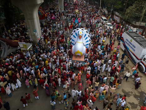 Dhaka Bangladesh 13 April 2026 Aerial view of a vibrant parade with a giant peacock float and dense crowds framed by metro pillars.