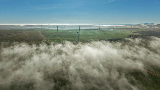 Aerial view of wind turbines standing in green fields partially obscured by low hanging clouds and mist in the rural landscape Vredenburg Western Cape South Africa. Aerial view of wind turbines standing in green fields partially obscured by low hanging clouds and mist in the rural landscape Vredenburg Western Cape South Africa.