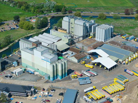 Aerial view of a large industrial facility with grain silos warehouses and yellow trucks parked in the yard near a canal in Little Irchester England United Kingdom. Aerial view of a large industrial facility with grain silos warehouses and yellow trucks parked in the yard near a canal in Little Irchester England United Kingdom.