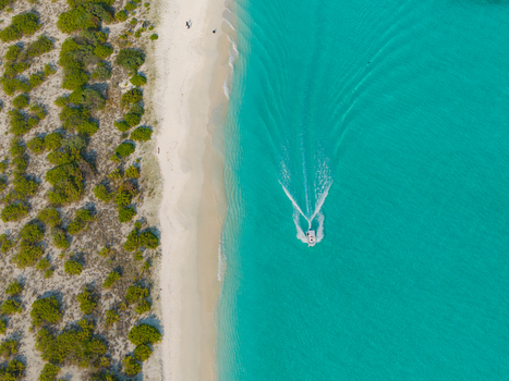 Aerial view of a speedboat cutting through the turquoise waters near a sandy beach fringed by lush greenery Dhidhdhoo Thiladhunmathi Atoll Maldives.