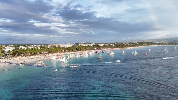 Malay Philippines 02 May 2026 Aerial view of Boracay Island featuring numerous traditional sailboats on turquoise waters along the sandy coastline lined with palm trees and resorts.
