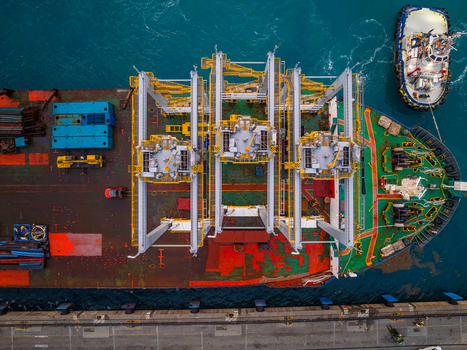 Aerial view of a cargo ship docked at the Caucedo Logistics Center with a tugboat alongside featuring large yellow gantry structures on deck in Andres Santo Domingo Dominican Republic. Aerial view of a cargo ship docked at the Caucedo Logistics Center with a tugboat alongside featuring large yellow gantry structures on deck in Andres Santo Domingo Dominican Republic.