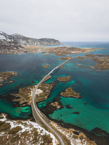 Aerial view of a bridge cutting through the turquoise water linking the islands in the Flakstadbruene region Flakstadbruene Nordland Norway. Aerial view of a bridge cutting through the turquoise water linking the islands in the Flakstadbruene region Flakstadbruene Nordland Norway.