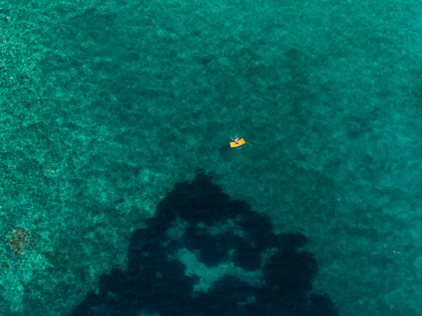 Aerial view of a person on a yellow float in the turquoise water of Aquarium Beach with visible underwater rock formations Jala Vlore County Albania. Aerial view of a person on a yellow float in the turquoise water of Aquarium Beach with visible underwater rock formations Jala Vlore County Albania.