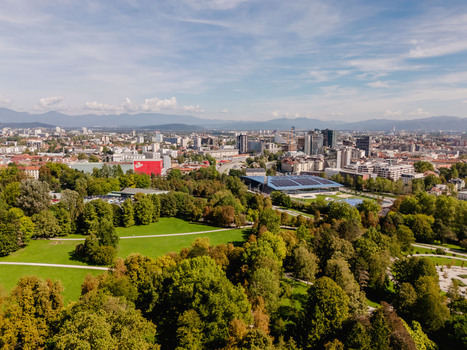 Aerial view of Tivoli Park with lush green trees walking paths and the city skyline of Ljubljana in the background under a clear blue sky in Ljubljana Slovenia.