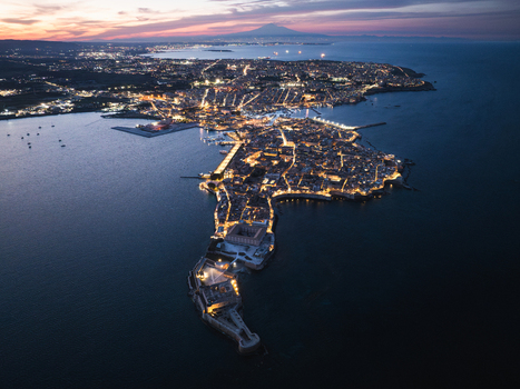 Aerial view of the Island of Ortigia at twilight with city lights reflecting on the water and Mount Etna in the background Syracuse Sicily Italy. Aerial view of the Island of Ortigia at twilight with city lights reflecting on the water and Mount Etna in the background Syracuse Sicily Italy.