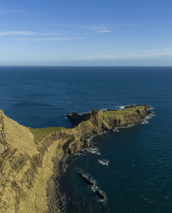 Aerial view of The Brother s Point headland with steep grassy cliffs and rocky shores under a clear blue sky in Culnacnoc Scotland United Kingdom. Aerial view of The Brother s Point headland with steep grassy cliffs and rocky shores under a clear blue sky in Culnacnoc Scotland United Kingdom.