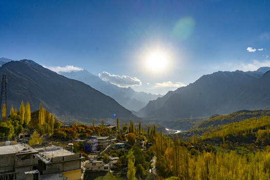 View of Hunza Valley featuring golden autumn foliage traditional architecture and dramatic mountain peaks under a clear blue sky in Karimabad Gilgit Baltistan Pakistan.