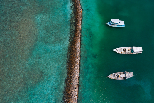 Aerial view of three boats anchored beside a stone breakwater in the clear turquoise waters of Kulhudhuffushi Haa Dhaalu Atoll Maldives. Aerial view of three boats anchored beside a stone breakwater in the clear turquoise waters of Kulhudhuffushi Haa Dhaalu Atoll Maldives.