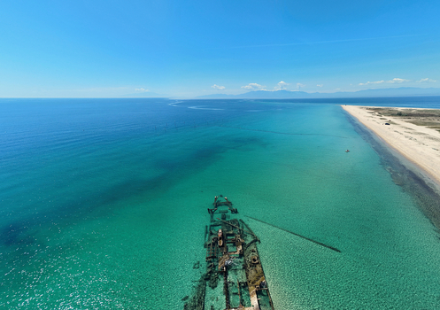 Aerial view of Shipwreck Epanomi submerged in turquoise waters along a sandy coastline under a clear blue sky Epanomi Greece.