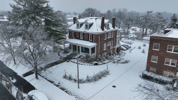 Aerial view of a historic brick house in the Rivermont neighborhood covered in fresh winter snow with surrounding trees and residential streets in Lynchburg Virginia United States.