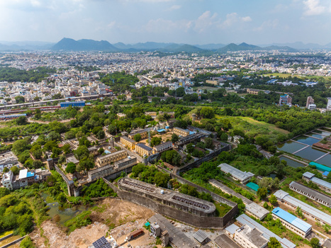 Aerial view of a historic fortified complex surrounded by lush greenery and stone walls with the urban landscape of Udaipur in the background Udaipur Rajasthan India. Aerial view of a historic fortified complex surrounded by lush greenery and stone walls with the urban landscape of Udaipur in the background Udaipur Rajasthan India.
