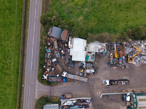 Aerial view of a chaotic scene of scrap metal and machinery contrasts with the adjacent lush green fields and the stark grey road Stafford England United Kingdom. Aerial view of a chaotic scene of scrap metal and machinery contrasts with the adjacent lush green fields and the stark grey road Stafford England United Kingdom.