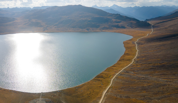 Aerial view of Sheosar Lake surrounded by golden brown meadows and distant mountain peaks with a dirt road running along the shoreline Skardu Gilgit Pakistan.