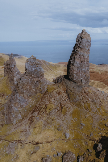 Aerial view of The Storr rock formations rising from the grassy slopes of the Isle of Skye with the sea in the background in Portree Scotland United Kingdom. Aerial view of The Storr rock formations rising from the grassy slopes of the Isle of Skye with the sea in the background in Portree Scotland United Kingdom.