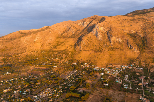Aerial view of Riserva Naturale Orientata dello Zingaro with rugged mountains golden sunset light and scattered residential houses in the valley San Vito Lo Capo Sicilia Italy. Aerial view of Riserva Naturale Orientata dello Zingaro with rugged mountains golden sunset light and scattered residential houses in the valley San Vito Lo Capo Sicilia Italy.