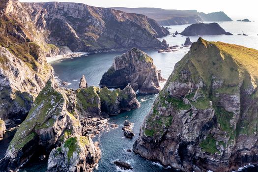 Aerial view of Glenlough Bay featuring dramatic rugged cliffs towering sea stacks and deep blue Atlantic waters along the coastline of Ardara County Donegal Ireland.