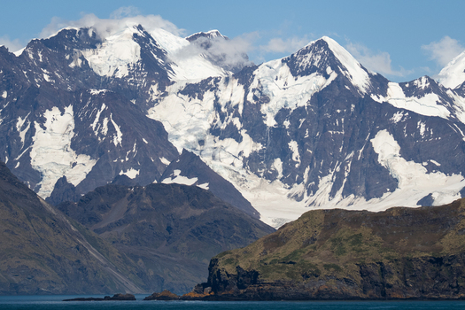View of the rugged snow capped mountains and glaciers rising above the rocky coastline in Grytviken South Georgia and the South Sandwich Islands. View of the rugged snow capped mountains and glaciers rising above the rocky coastline in Grytviken South Georgia and the South Sandwich Islands.