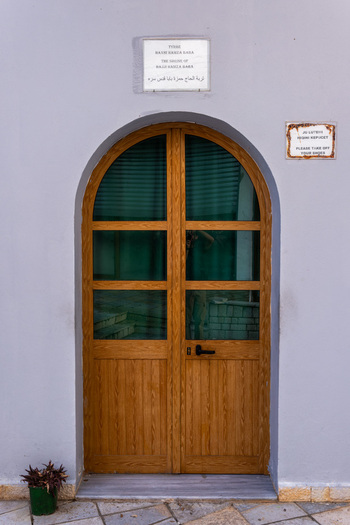 View of the arched wooden entrance to the Shrine of Hadji Hamza Baba with glass panels and a commemorative plaque on a purple wall in Kruje Durres County Albania.