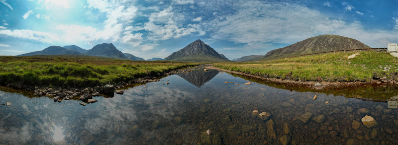 Aerial view of Buachaille Etive Mor mountain reflected in a stream surrounded by lush green highlands and a vast blue sky in Ballachulish Scotland United Kingdom. Aerial view of Buachaille Etive Mor mountain reflected in a stream surrounded by lush green highlands and a vast blue sky in Ballachulish Scotland United Kingdom.