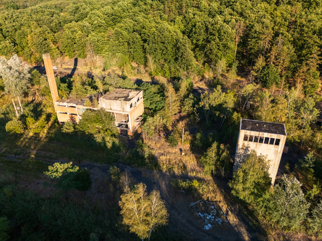 Aerial view of abandoned coal loading facility ruins surrounded by summer forest in Rakoczibanya Hungary with a tall brick chimney and overgrown industrial buildings. Aerial view of abandoned coal loading facility ruins surrounded by summer forest in Rakoczibanya Hungary with a tall brick chimney and overgrown industrial buildings.