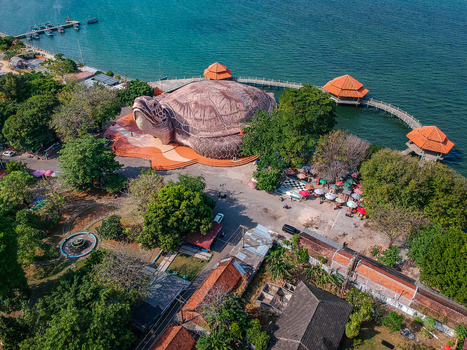 Aerial view of the giant turtle shaped building of Kura Kura Ocean Park on the coastline with wooden walkways and gazebos over turquoise water in Jepara Central Java Indonesia. Aerial view of the giant turtle shaped building of Kura Kura Ocean Park on the coastline with wooden walkways and gazebos over turquoise water in Jepara Central Java Indonesia.