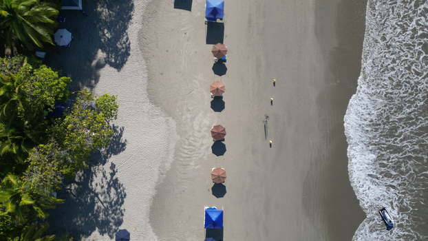 Aerial view of the beach with colorful umbrellas casting shadows on the sand as the waves crash on the shore Quepos Puntarenas Province Costa Rica. Aerial view of the beach with colorful umbrellas casting shadows on the sand as the waves crash on the shore Quepos Puntarenas Province Costa Rica.