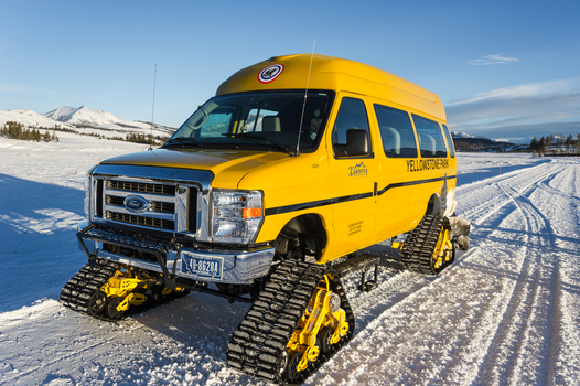 View of a yellow snow coach vehicle with tracks parked on a snow covered road in Yellowstone National Park United States.
