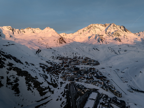 Aerial view of snow capped peaks kissed by the rising sun s glow over a village nestled in the valley Val Thorens Auvergne Rh&ocirc;ne Alpes France.