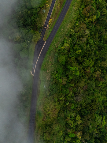 Aerial view of a winding asphalt road passing through dense tropical forest partially covered by thick white mist in Cinchona Alajuela Province Costa Rica. Aerial view of a winding asphalt road passing through dense tropical forest partially covered by thick white mist in Cinchona Alajuela Province Costa Rica.