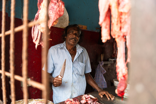 Sri Lanka 18 February 2026 View of a butcher holding a knife in a traditional meat shop with raw meat hanging from hooks and rustic walls.